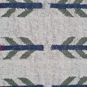 May include: Close-up of a woven textile with a repeating pattern of stylized arrows. The arrows feature red, gold, and blue elements against a neutral, textured background. The textile appears to be made of natural fibers.