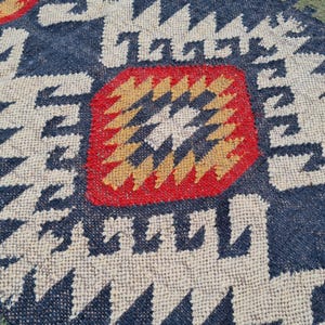 May include: Close-up of a woven rug with a geometric pattern. The rug features a navy blue background with white, red, and yellow geometric shapes. The edges are green.