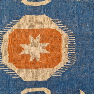 Puede incluir: Textil azul con un patr&oacute;n repetitivo de formas geom&eacute;tricas. El dise&ntilde;o incluye oct&aacute;gonos naranjas con estrellas blancas, rodeados de l&iacute;neas blancas y formas de estrellas blancas. El fondo es de color azul liso.