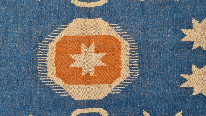 Puede incluir: Textil azul con un patr&oacute;n repetitivo de formas geom&eacute;tricas. El dise&ntilde;o incluye oct&aacute;gonos naranjas con estrellas blancas, rodeados de l&iacute;neas blancas y formas de estrellas blancas. El fondo es de color azul liso.