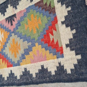 Puede incluir: Una alfombra rectangular con un patr&oacute;n geom&eacute;trico. La alfombra presenta un borde azul marino y un dise&ntilde;o central con diamantes en varios colores, incluyendo azul, naranja, rojo y rosa. La alfombra tiene un borde con flecos.