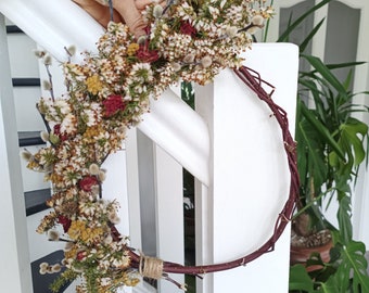 Corona de flores secas con brezo blanco, flores de sauce y claveles en un anillo de sauce natural.