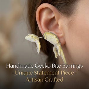 Op de afbeelding: Handgemaakte Gecko Bite oorbellen. Deze unieke oorbellen hebben een gecko-ontwerp in een lichtbeige kleur met gele accenten. De oorbellen zijn ambachtelijk vervaardigd en zijn een uniek statement-stuk.