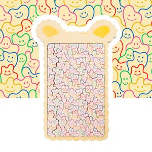 May include: A light yellow puzzle with a scalloped edge and a bear-shaped top. The puzzle features a pattern of smiling, colourful, abstract figures. The background shows a similar pattern of smiling figures in various colours.