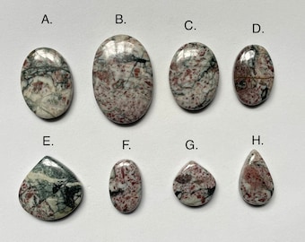 May include: Eight cabochon gemstones in various shapes and sizes, including oval, teardrop, and round. The stones are a mix of white, gray, and red with a marbled pattern.