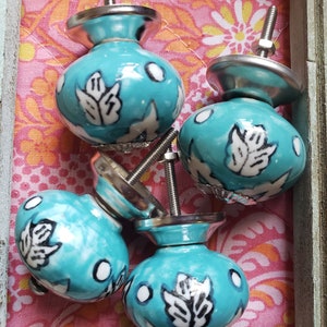 May include: Four turquoise ceramic cabinet knobs with white floral designs. The knobs have a silver metal base and screw.