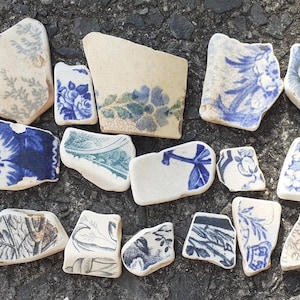Puede incluir: Una colección de diecisiete fragmentos de cerámica irregulares con diversos patrones florales, botánicos y geométricos en azul y blanco. Estos trozos de cerámica rota muestran motivos decorativos variados, incluyendo flores, hojas y enredaderas intrincadas sobre fondo blanco.