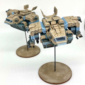 Könnte beinhalten: Zwei beige und blaue Miniatur-Raumschiffe mit detaillierter Bemalung, montiert auf runden Sockeln.