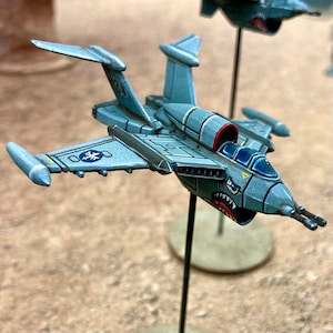 May include: A gray and blue miniature spaceship with a red and white cockpit and a toothy, cartoonish face painted on the front. The spaceship is mounted on a black stand.