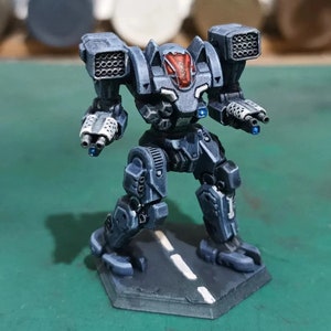 May include: A detailed miniature robot model in shades of grey and blue, with red accents on the head. The model features missile launchers and gun barrels, standing on a hexagonal base with a road design. The robot is a detailed representation of a mech.