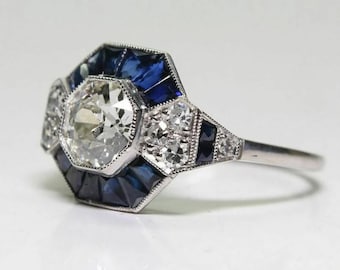 May include: A vintage-style ring with a large, octagonal-shaped diamond surrounded by smaller diamonds and blue sapphires. The ring is set in platinum.