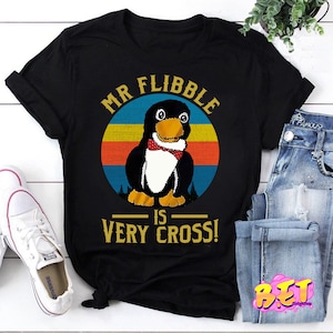 May include: Black t-shirt with a retro-style graphic of a penguin wearing a bow tie. The text "Mr. Flibble is Very Cross!" is printed on the shirt.