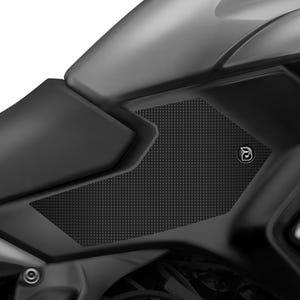 May include: Close-up of a black motorcycle tank protector with a textured surface. The protector has a small, silver logo with the letter "B" on it.