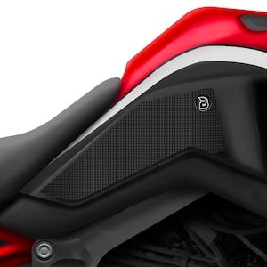 Pode incluir: Um protetor de tanque de motocicleta preto com uma superfície texturizada e um pequeno logotipo no canto superior direito. O protetor está instalado em um tanque de motocicleta vermelho.