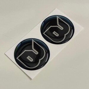 May include: Two black and silver round stickers with the letter "B" in a stylized font.