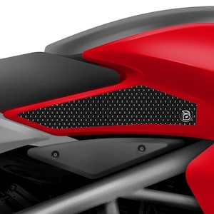 Puede incluir: Un protector de tanque de motocicleta negro con un patrón texturizado y un pequeño logotipo. El protector está instalado en un tanque de motocicleta rojo.