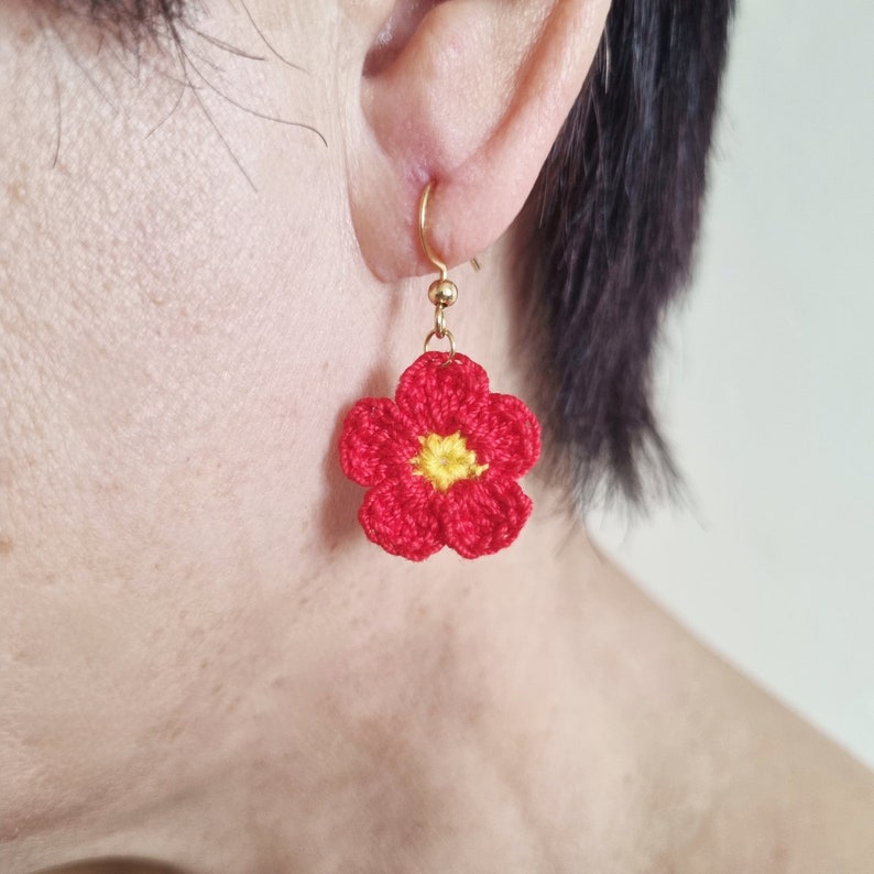 May include: Red crocheted flower earrings with a yellow center. The earrings are hanging from gold hooks.