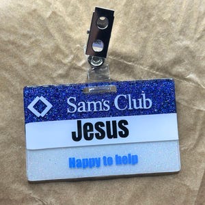 May include: A blue and white glitter name tag with the text "Sam's Club" and "Jesus" in black text. The tag also has the text "Happy to help" in blue text.