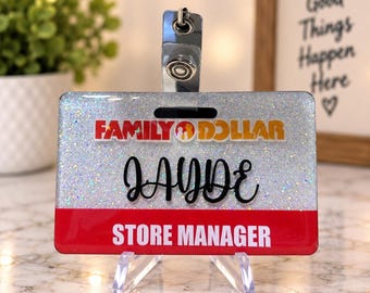 May include: A rectangular badge holder featuring a silver glitter background with the Family Dollar logo at the top. The name JAYDE is written in black script in the centre, and a red horizontal bar at the bottom displays STORE MANAGER in white.