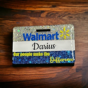 May include: A blue and silver glitter name tag with the Walmart logo and the text "Our people make the difference". The name tag has a white nameplate with the name "Darius" printed in black.