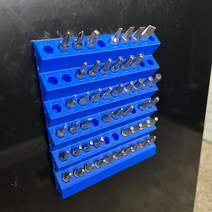 May include: A blue magnetic wall mount organizer with a variety of silver screwdriver bits. The organizer has multiple rows of hexagonal slots to hold the bits.