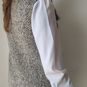 May include: A brown and white tweed waistcoat with a white blouse underneath.