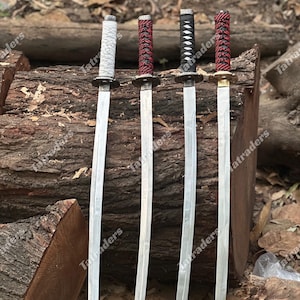 May include: Four katana swords with silver blades and wrapped handles in white, red, and black. The swords are displayed on a wooden log, showcasing their traditional design and craftsmanship.