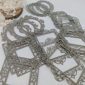 Pode incluir: Um conjunto de molduras de papel decorativas cinzas com designs intrincados. As molduras são feitas de um material delicado e rendado, perfeitas para adicionar um toque de elegância a qualquer projeto.