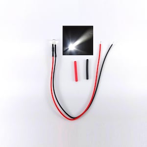 Könnte beinhalten: Eine kleine, transparente LED mit roten und schwarzen Drähten sowie eine Nahaufnahme des Lichts, das einen hellen Strahl aussendet. Zwei kleine, farbige Röhrchen sind ebenfalls vorhanden. Die Komponenten sind vor einem weißen Hintergrund angeordnet.