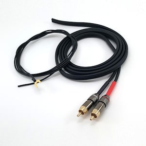 Può includere: Un cavo audio nero con due connettori RCA dalle punte dorate, uno contrassegnato da un manicotto rosso e l'altro da un manicotto nero. Un sottile filo nero separato con un terminale a forcella color oro è fissato al cavo principale.