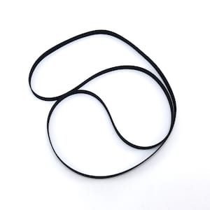Op de afbeelding: Een zwarte rubberen riem, waarschijnlijk voor een vintage audio-apparaat, wordt getoond tegen een witte achtergrond. De riem is in een achtvormige lus gelegd. De gladde textuur en donkere kleur van de riem contrasteren met de heldere achtergrond.