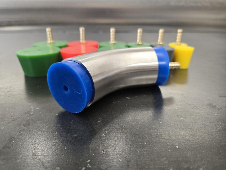 May include: A stainless steel curved pipe with blue rubber ends and a small hole. Several colorful rubber stoppers with brass fittings are in the background. The stoppers are green, red, and yellow.