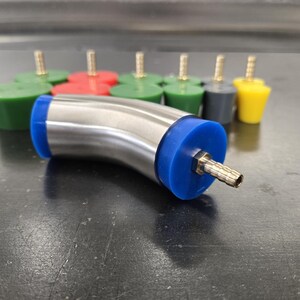 May include: A stainless steel elbow fitting with blue rubber ends and a brass nozzle is in the foreground. Several colored rubber stoppers with brass stems are in the background. The stoppers are green, red, gray, and yellow.