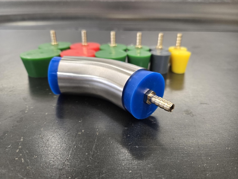 May include: A stainless steel elbow fitting with blue rubber ends and a brass nozzle is in the foreground. Several colored rubber stoppers with brass stems are in the background. The stoppers are green, red, gray, and yellow.