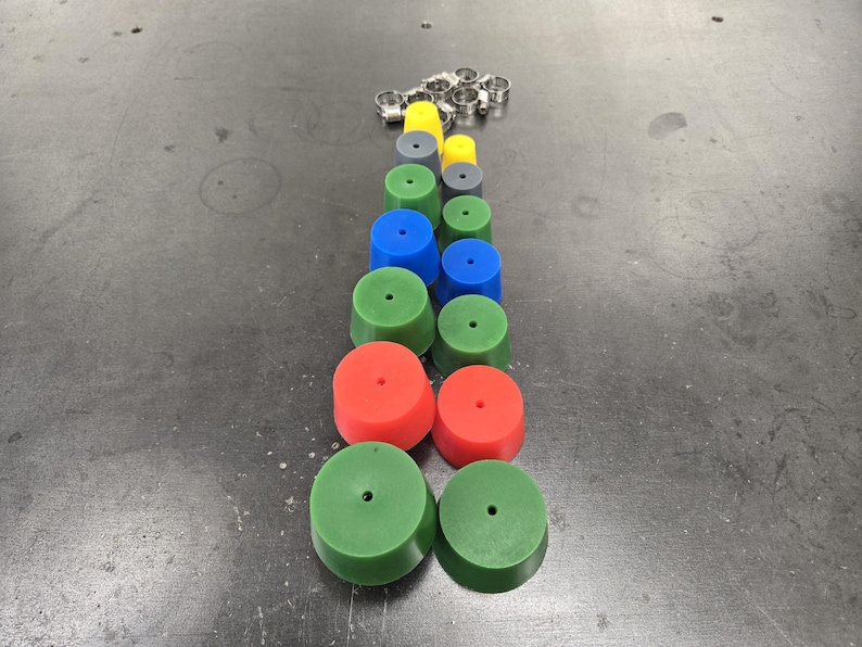 May include: An assortment of colorful, cylindrical objects in red, green, blue, yellow, and gray, with a small hole in the center of each. Several silver metal clamps are also present. The objects are arranged in a vertical line.