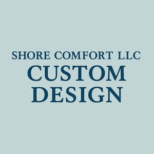 May include: A light blue background with the text "SHORE COMFORT LLC" in a dark blue serif font above the words "CUSTOM DESIGN" in a larger, darker blue serif font.