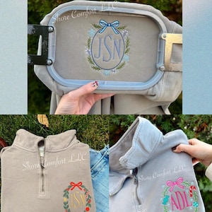 May include: A light gray quarter-zip sweatshirt with embroidered initials inside a wreath design. The sweatshirt is shown in different stages of the embroidery process. The text "Shore Comfort LLC" is visible on the sweatshirt.