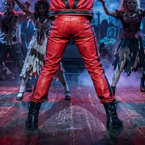May include: Bright red leather pants featuring a black vertical stripe down each leg, a black waistband, and back pockets. The pants are paired with black leather lace-up boots, showcasing a bold, structured design with visible stitching details.