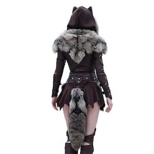 May include: A brown faux leather and suede costume with a wolf theme. The outfit includes a hooded jacket with faux fur trim, a matching skirt, and a tail. The sleeves have decorative detailing, and the boots are brown.