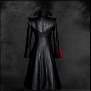 Pu&ograve; includere: Un lungo cappotto di pelle nera con un colletto alto e dettagli rossi sui polsini. Il cappotto ha un corpetto aderente e una gonna fluida.