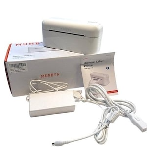 Puede incluir: Una impresora de etiquetas térmica MUNBYN blanca, con su caja, adaptador de corriente y manual de usuario. La caja tiene el logotipo de MUNBYN en rojo. La impresora es blanca con el logotipo de MUNBYN en negro. El manual es blanco con "thermal label printer".