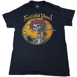 May include: Black t-shirt featuring a circular graphic with the words "Grateful Dead" above a skeleton with a floral crown. The graphic is in shades of yellow, orange, and red. The shirt has a crew neck and short sleeves.