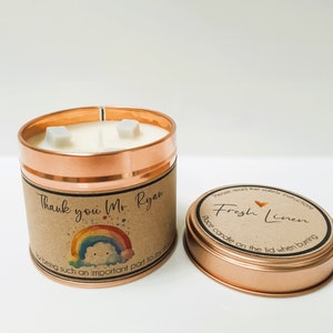 May include: A copper candle tin with a brown label that says "Thank you Mr. Ryan for being such an important part to my story." The candle has white wax with three wicks. The lid of the tin is copper and has a brown label that says "Please read the safety instructions Fresh Linen Place candle on the lid when burning."
