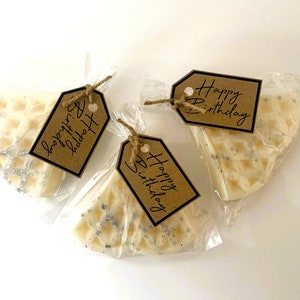 Peut inclure: Trois petites bougies blanches en forme de gaufre avec un motif de paillettes argent&eacute;es, chacune emball&eacute;e dans un sac en plastique transparent avec une &eacute;tiquette en papier brun. Les &eacute;tiquettes portent le texte "Happy Birthday" &eacute;crit en noir.