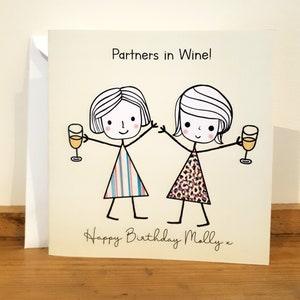 Peut inclure: Une carte d'anniversaire avec une illustration de deux amies levant un verre de vin. La carte indique "Partners in Wine!" et "Happy Birthday Molly x".