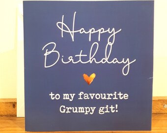May include: A blue card with white text that reads "Happy Birthday to my favourite Grumpy git!" with a gold heart in the middle.