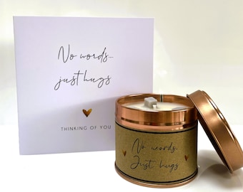 May include: A brown candle with a copper lid and a gold heart design. The candle has the text "No words... Just hugs" on the label. The candle is next to a white card with the text "No words... Just hugs" and "Thinking of you".