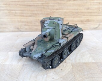 May include: A green and brown camouflage painted model tank with a raised gun turret. The tank has a detailed track system and is made of plastic.