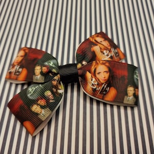 May include: A black and white bow with a red, orange, and yellow print of the characters from the TV show "Buffy the Vampire Slayer".