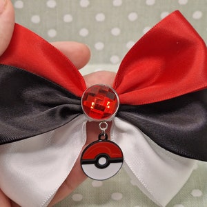 May include: A red, black and white ribbon bow with a red gem and a Pokeball charm.